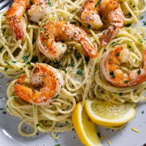 pea pasta on a white plate with shrimp and lemon wedges