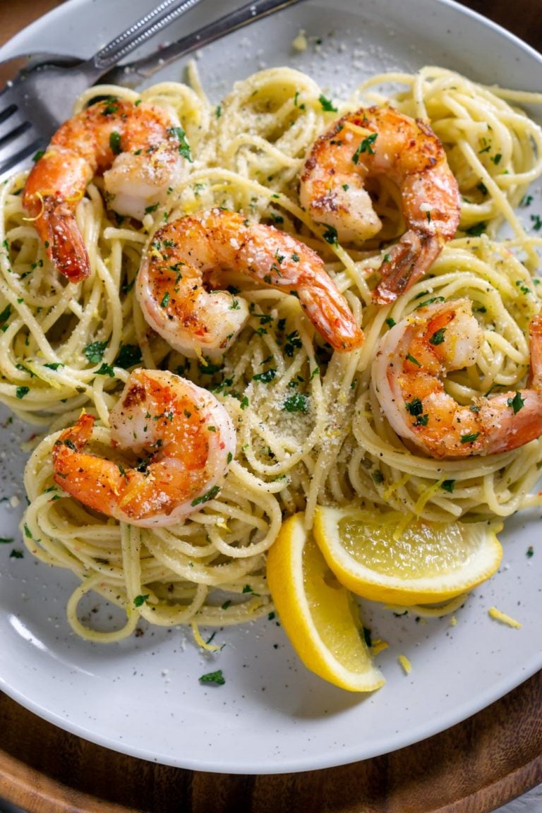 pea pasta on a white plate with shrimp and lemon wedges