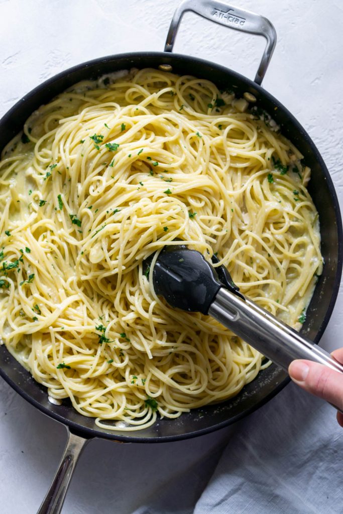 tongs mixing pasta in a large black pan