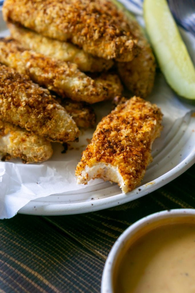 air fryer chicken tenders on a plate and one with a bite taken