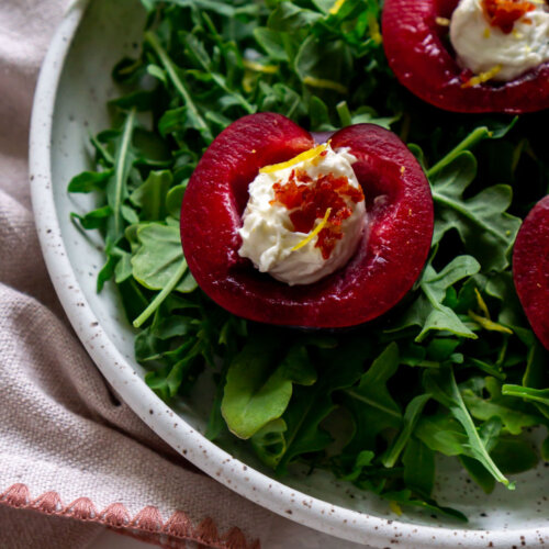 stuffed plums over arugula in a white bowl