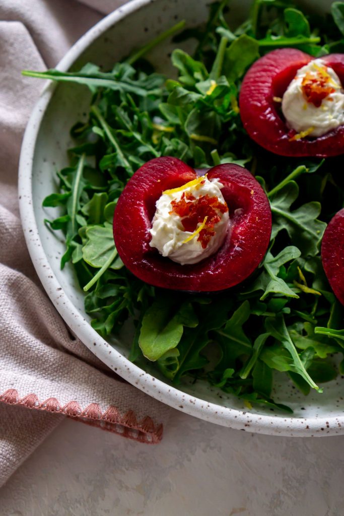 stuffed plums over arugula in a white bowl