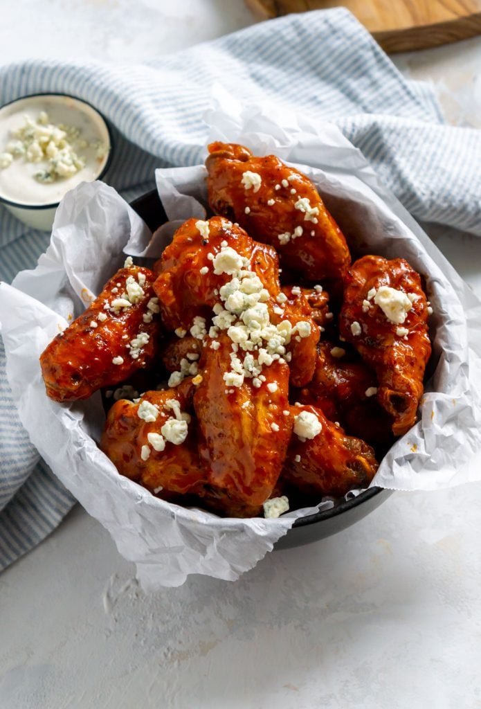 air fryer buffalo wings in a bowl with parchment paper and a striped napkin
