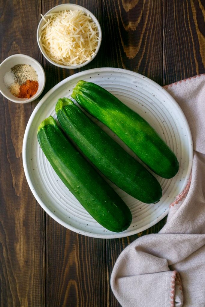 three zucchini on a white plate with parmesan cheese