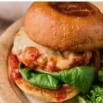 A chicken parmesan burger on a toasted bun with fresh basil.