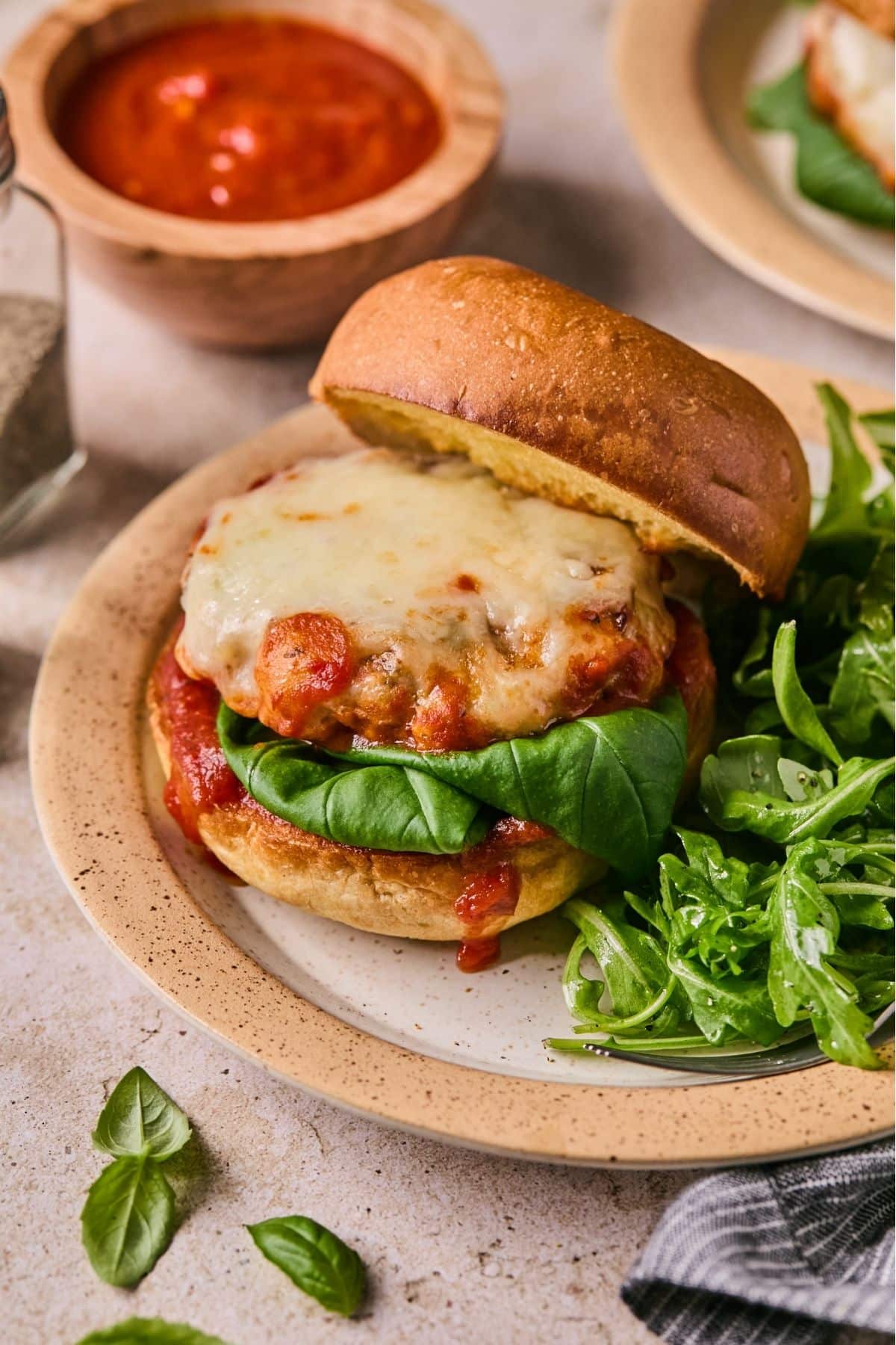 Cooked chicken parm burger in a bun on a ceramic plate.