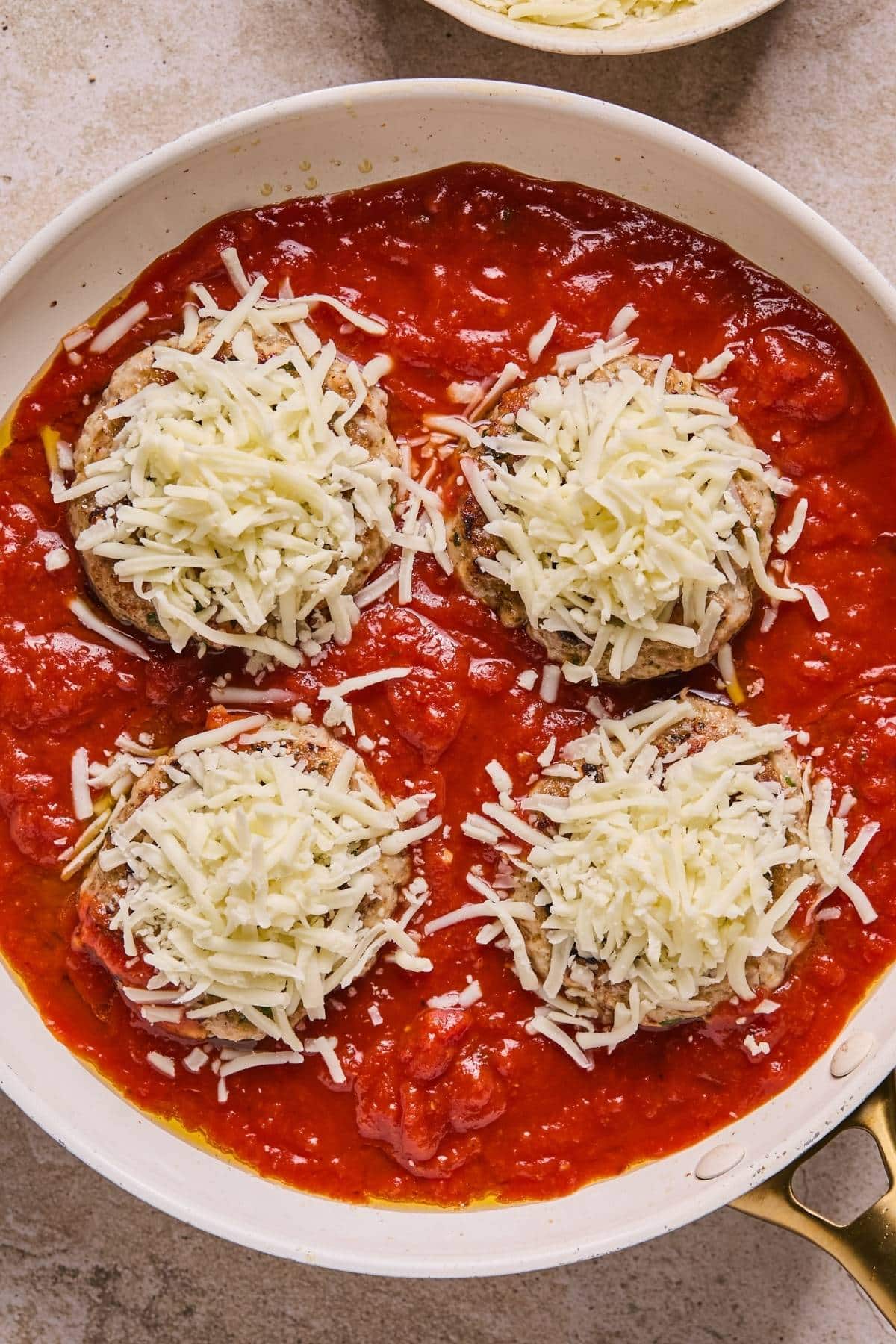 Chicken patties in marinara sauce with shredded cheese on top.