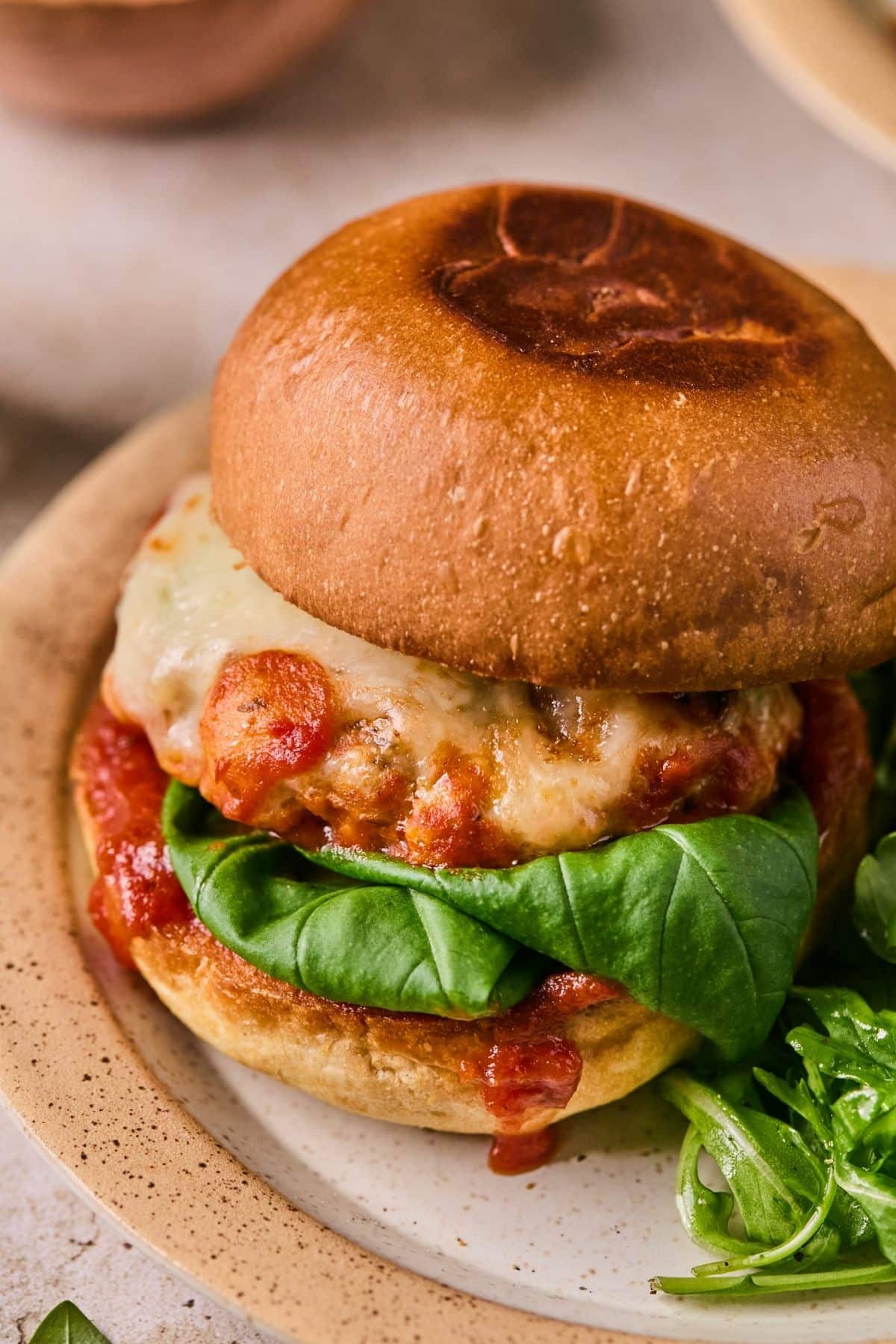 A chicken parmesan burger on a bun on a ceramic dish with a side salad.