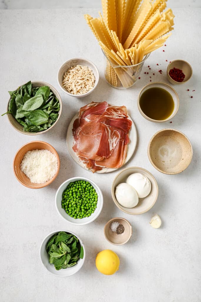 pasta, mint, prosciutto, parmesan cheese, peas, burrata, and basil in small ingredient bowls