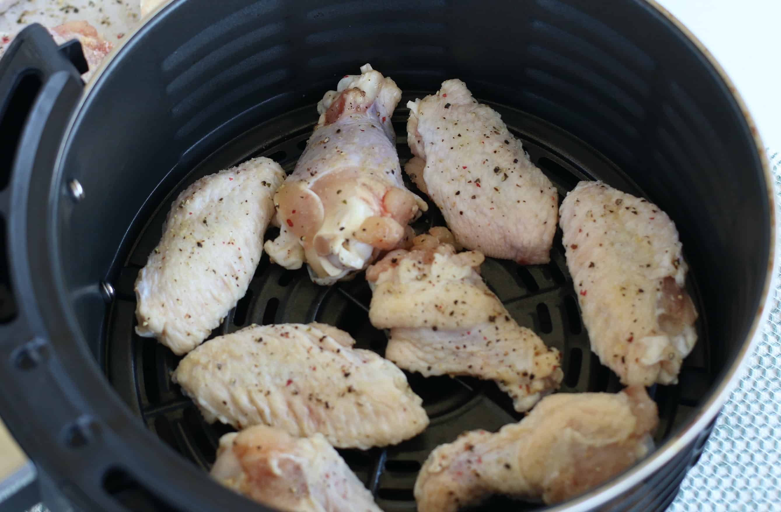 Seasoned chicken wings in an air fryer basket arranged in a single layer.