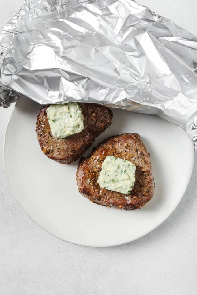 Rested steaks topped with melting blue-cheese butter under foil.