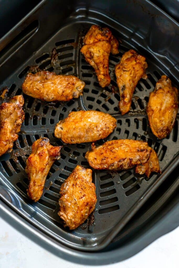 Cooked chicken wings in an air fryer basket.