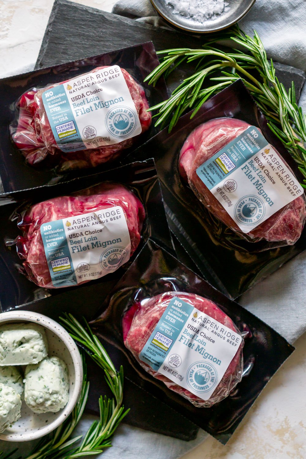 Sealed packs of filet mignons on a counter with a bowl of blue cheese butter.