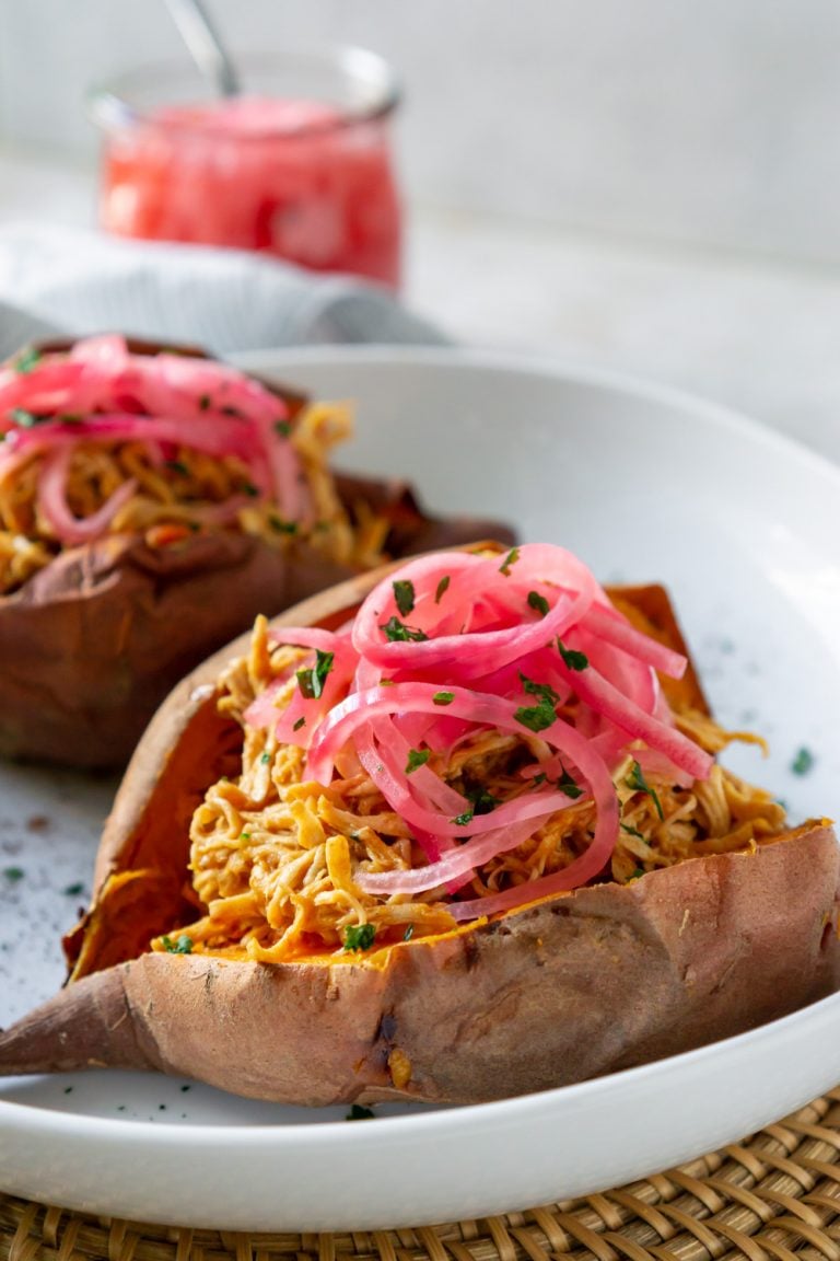 Bbq chicken stuffed sweet potato on a white plate next to a jar of pickled red onions.