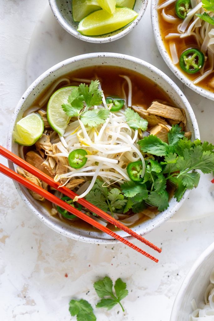 chicken pho in a white bowl with red chopsticks
