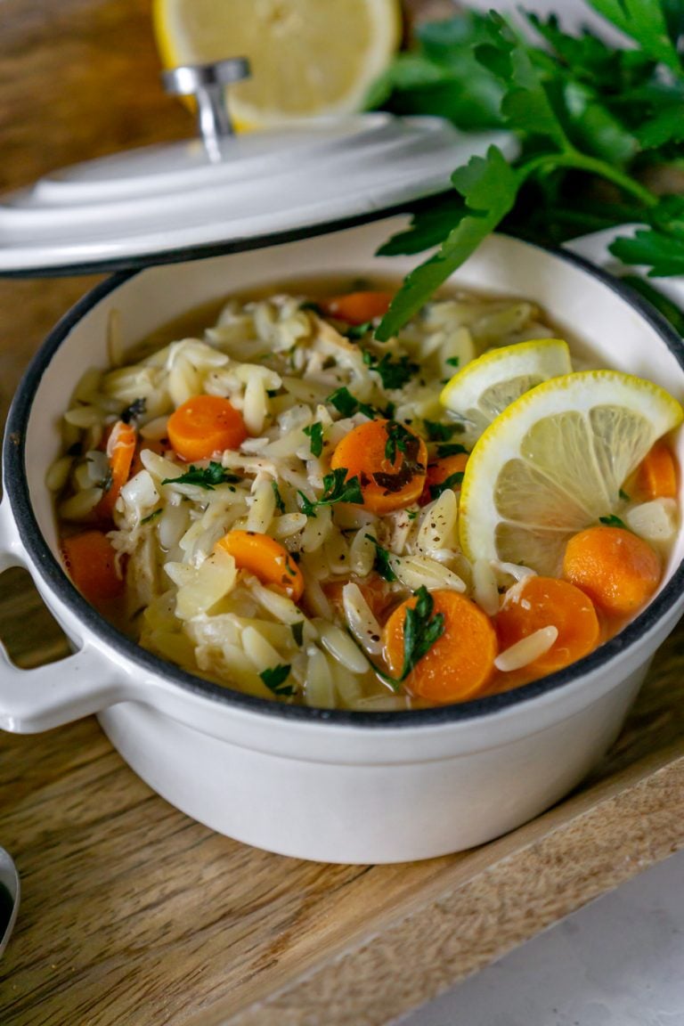 lemon orzo soup in a white bowl with lemon slice