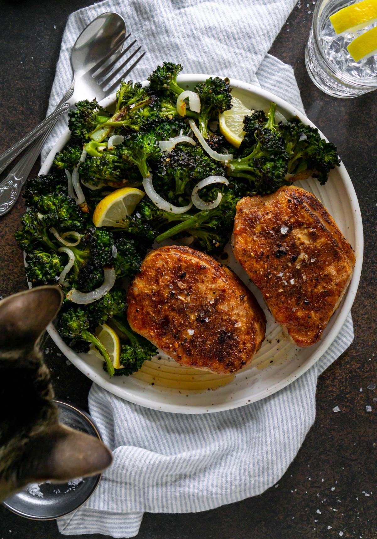 two juicy air fryer boneless pork chops on a plate with broccolini and a cat peeking over the plate
