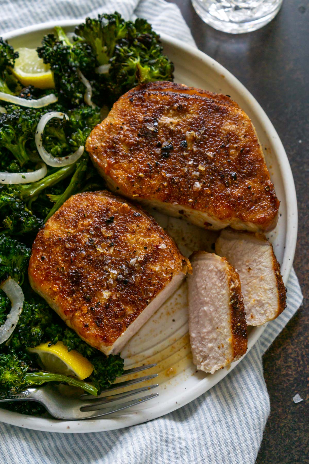 sliced pork chops after air frying on a white plate with a fork next to a side of broccolini
