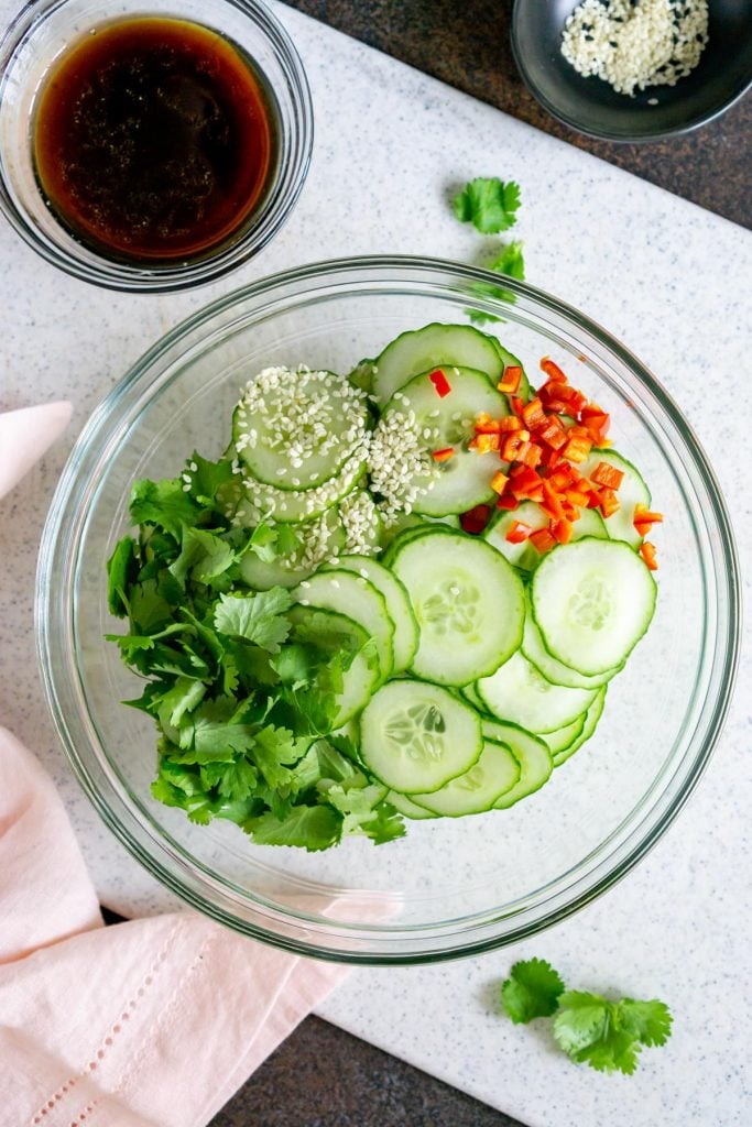 cucumbers, chili peppers, cilantro, and sesame seeds in a glass bowl