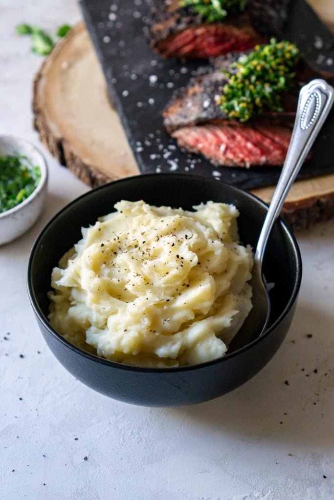 mashed potatoes in a black bowl, steak in the background