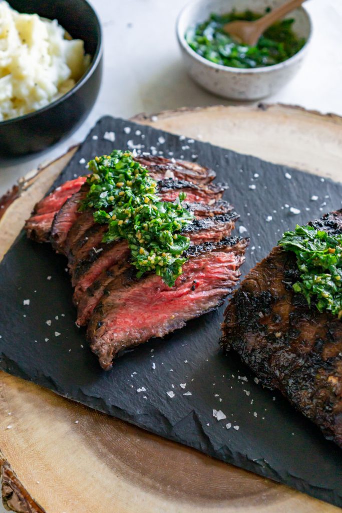 sliced chimichurri steak on a black serving board