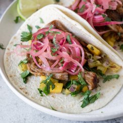 two carnitas tacos on a white plate with lime wedges