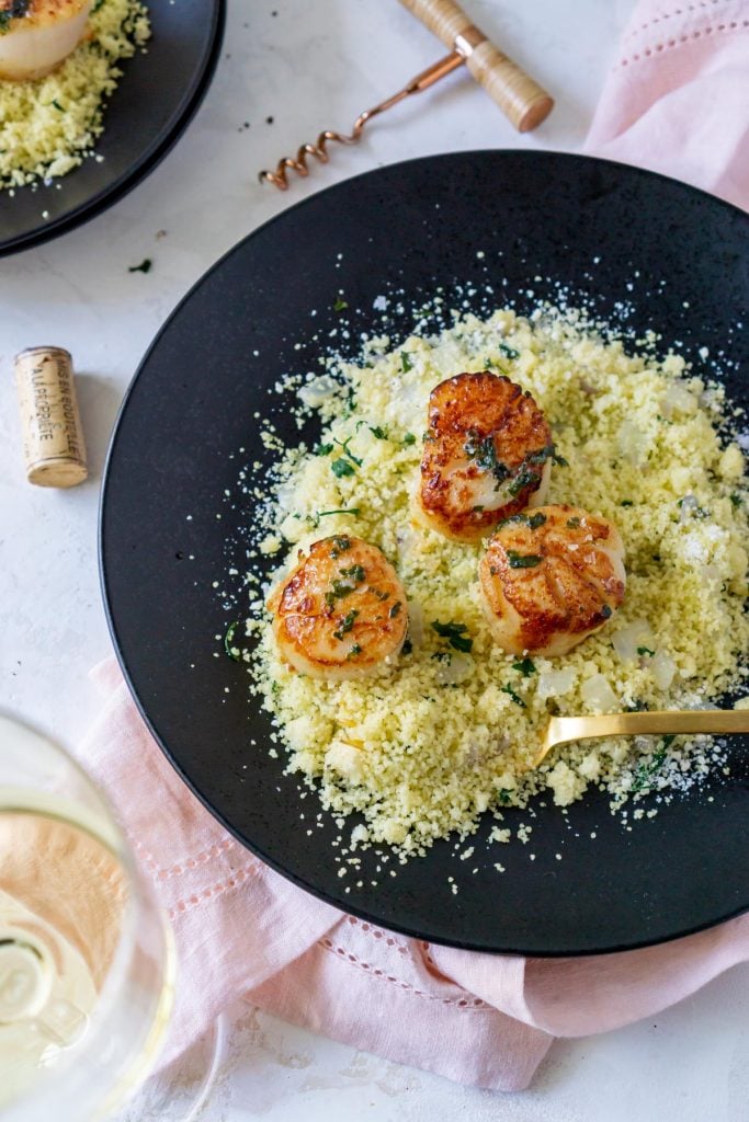 moroccan couscous on a black plate with seared scallops