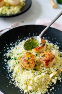 spoon drizzling basil butter over seared scallops