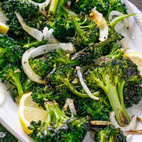 broccolini on a plate with onions and lemon wedges