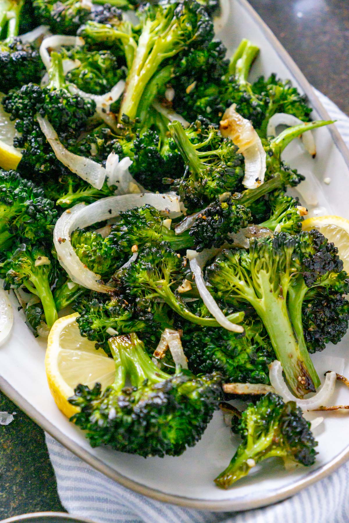 Broccolini on a plate with onions and lemon wedges.