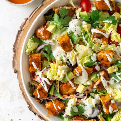 crispy buffalo chicken salad in a large white bowl with buffalo sauce on the side