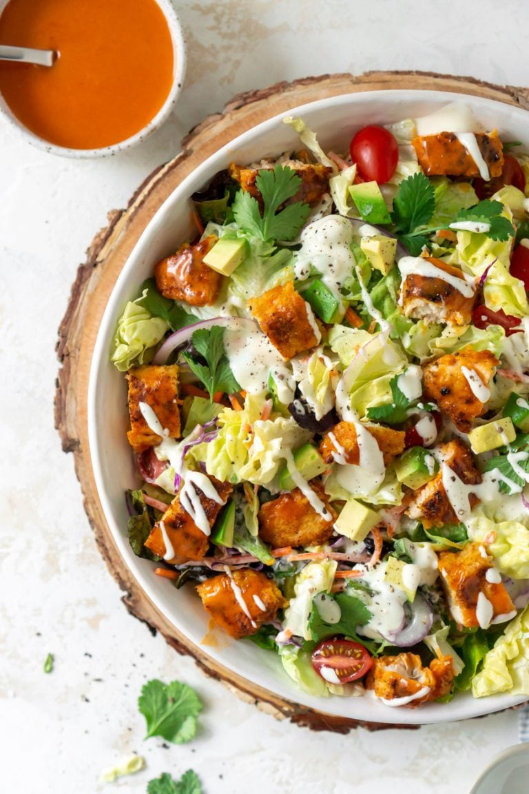 crispy buffalo chicken salad in a large white bowl with buffalo sauce on the side