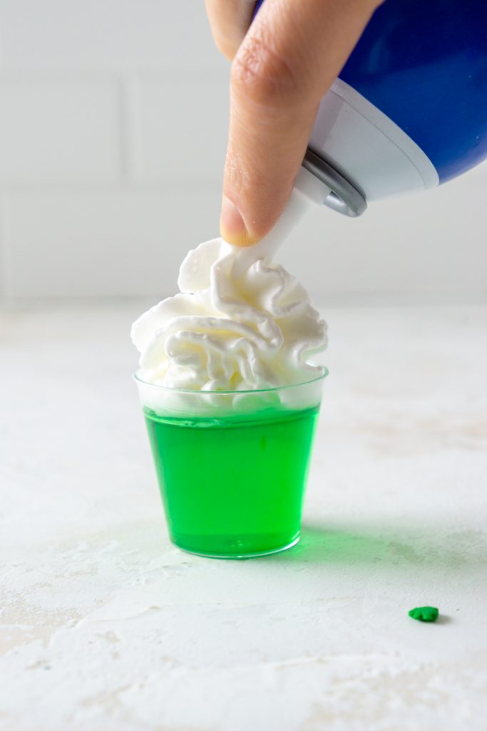 putting whipped cream on top of a green jello shot