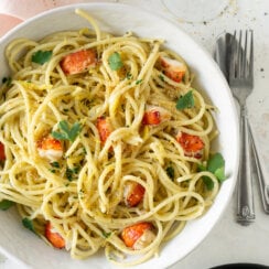 lobster pasta in a white bowl with a silver fork and wine