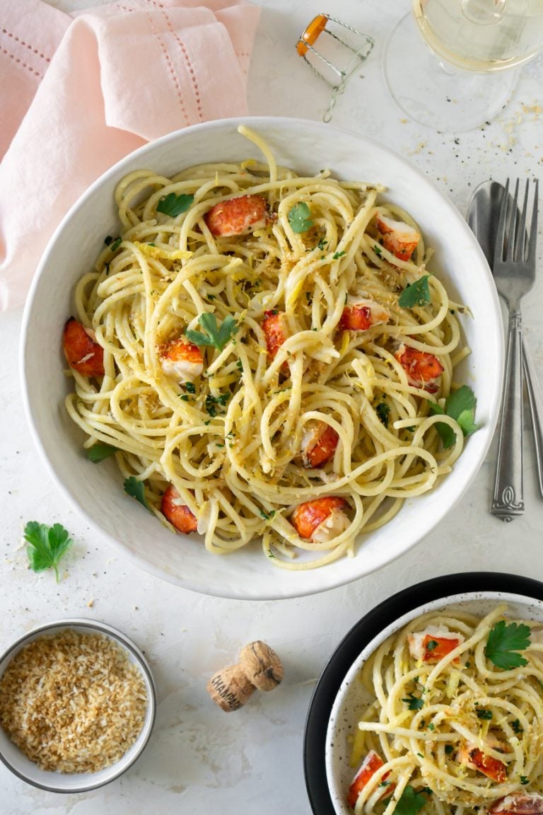 pasta in a big bowl and on a small plate with silverware and wine