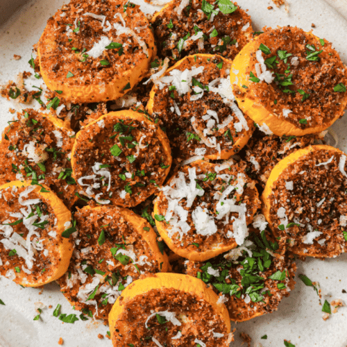 roasted yellow squash on a white plate topped with cheese and parsley