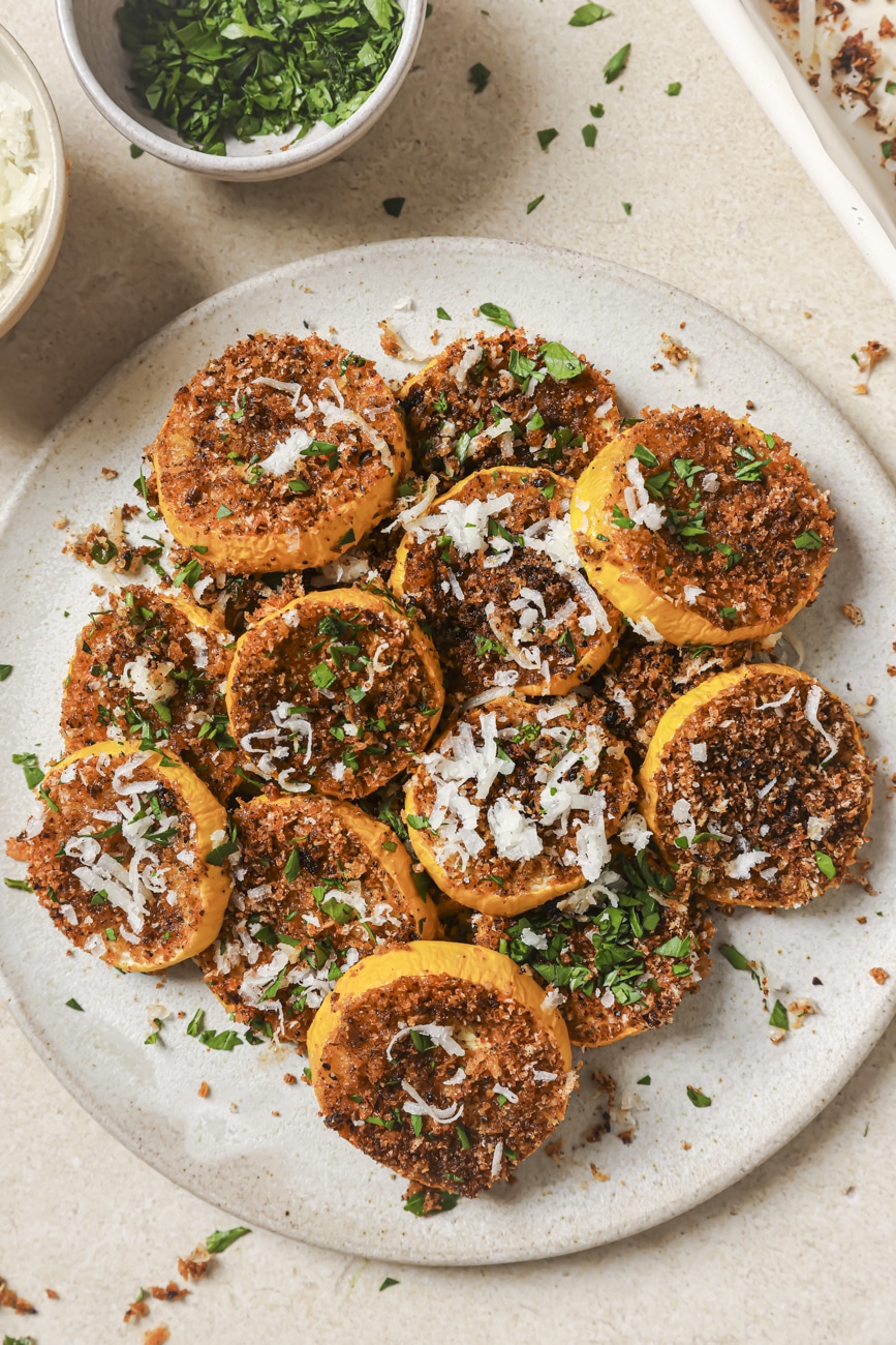 roasted yellow squash on a white plate topped with cheese and a bowl of parsley on the side.