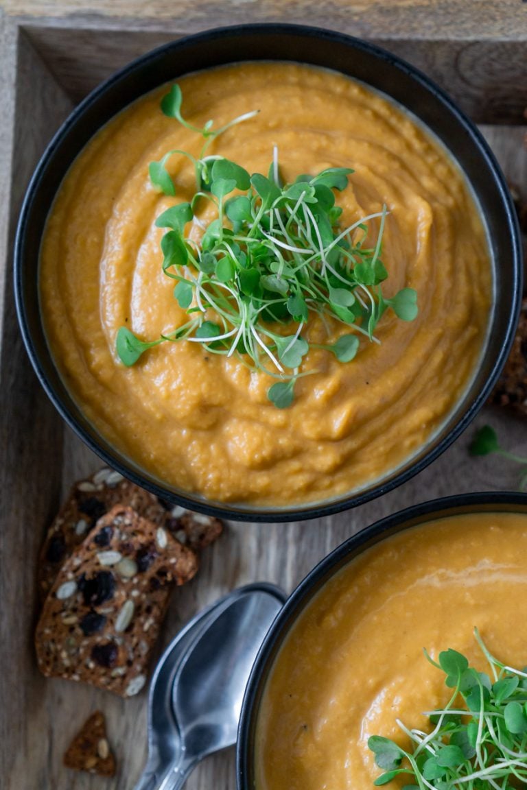 roasted butternut squash soup in a black bowl with micro greens