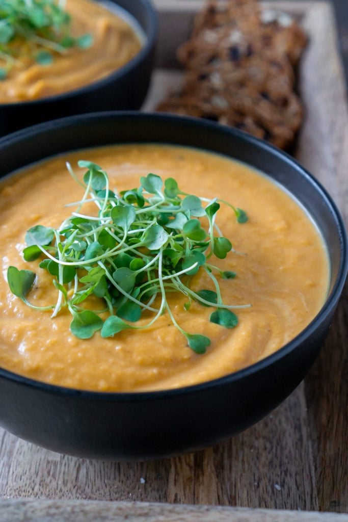 roasted butternut squash soup in a black bowl with micro greens