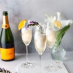 3 champagne cocktails on a wood serving board with flowers