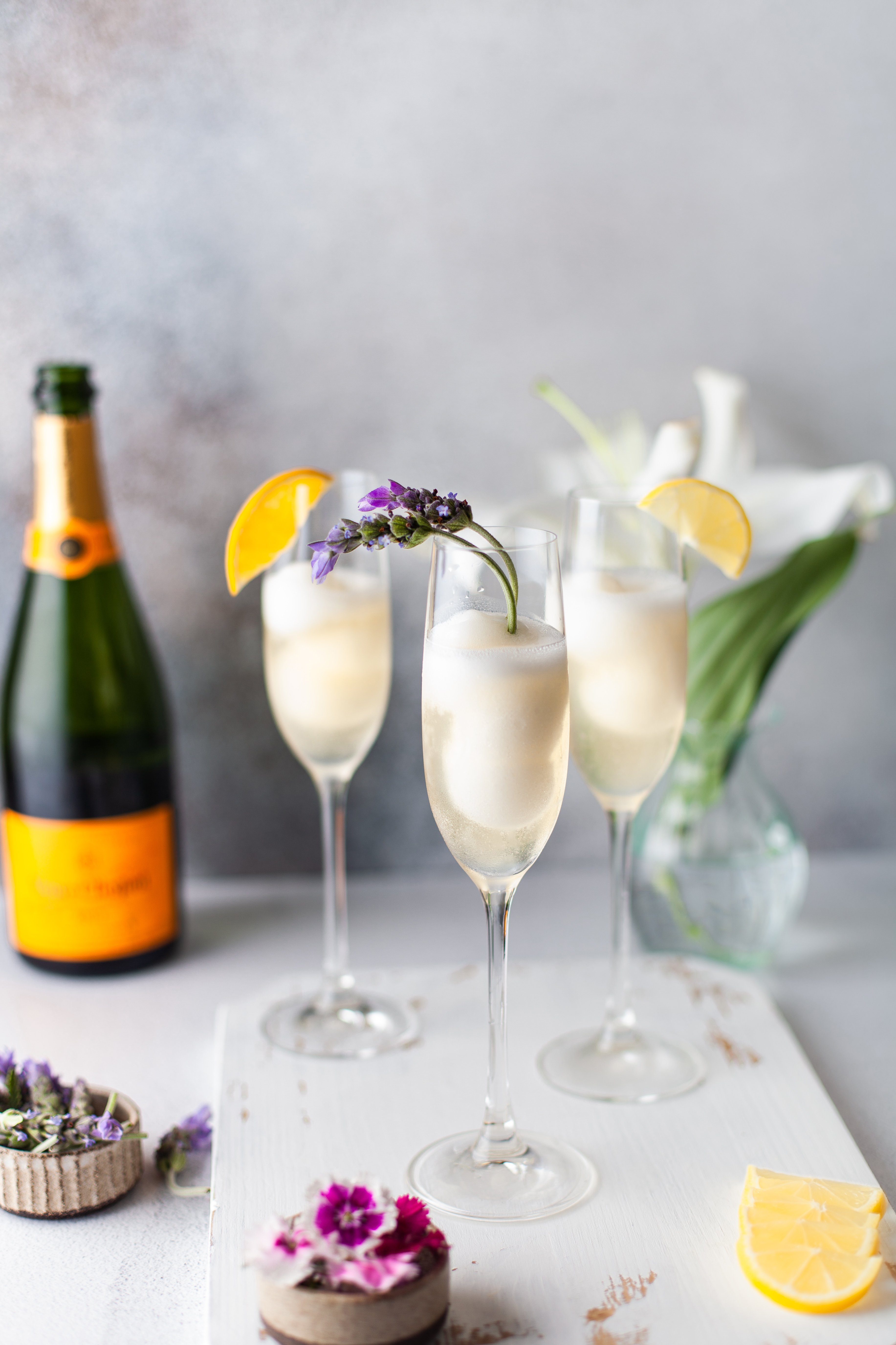 3 champagne cocktails on a wood serving board with flowers
