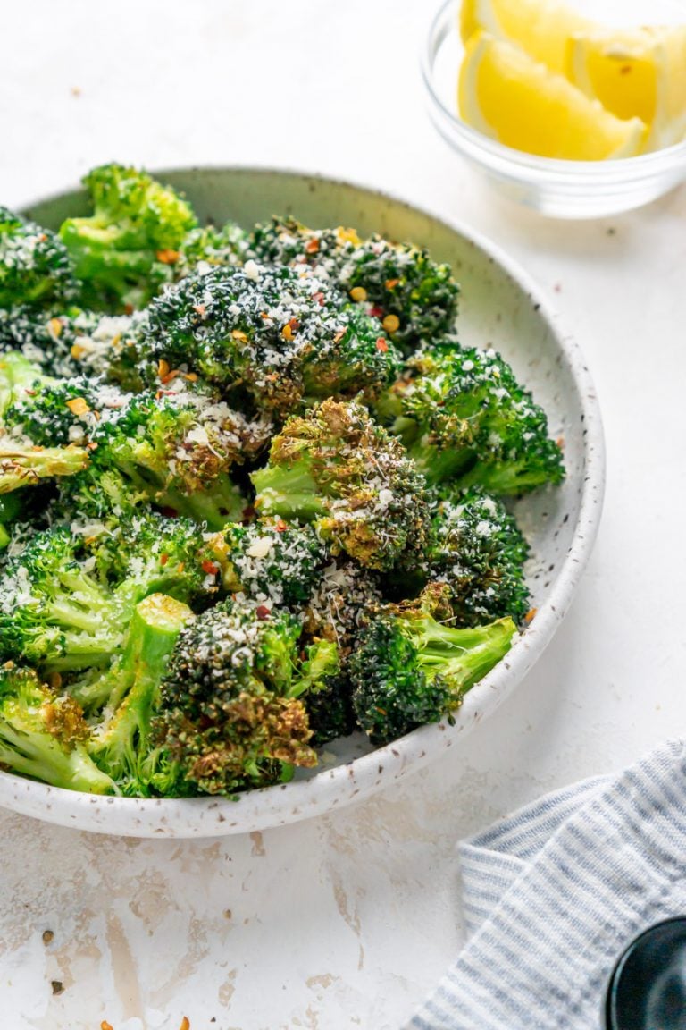 air fryer broccoli in a white bowl and lemon wedges