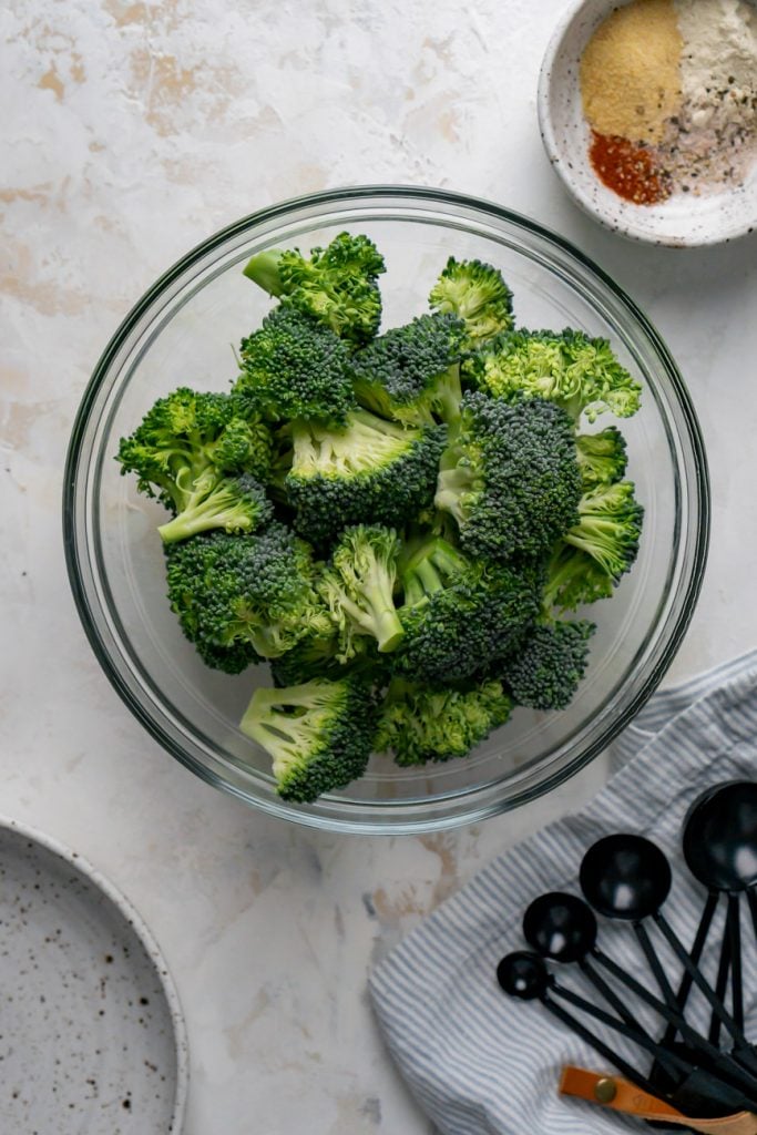 broccoli florets in a glass bowl, seasoning, and black measuring spoons