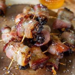 bacon wrapped dates on a wood serving tray with honey