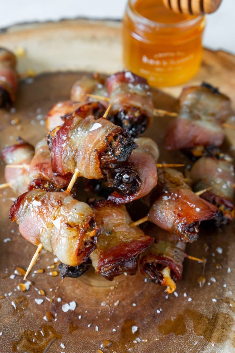 bacon wrapped dates on a wood serving tray with honey