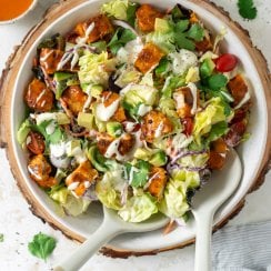 buffalo chicken salad in a salad bowl with tongs and a blue napkin
