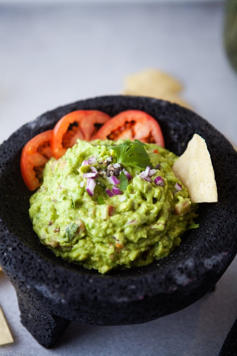 gaucamole with a chip and sliced tomatoes in a molcajete