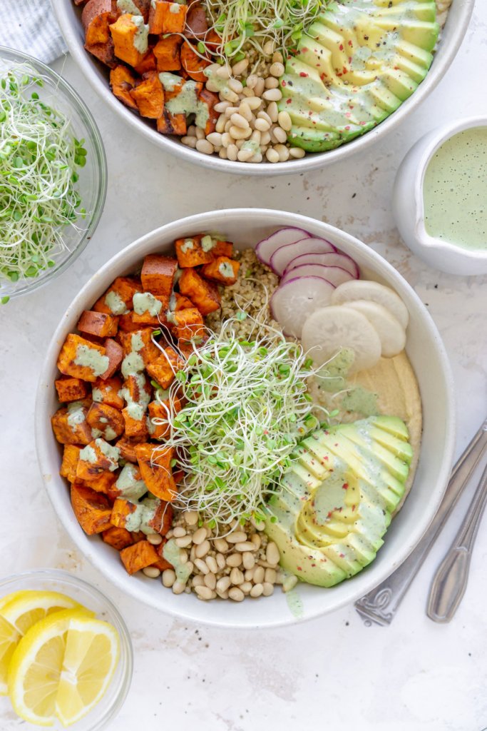 two sweet potato bowls with lemon wedges and dressing in a bowl