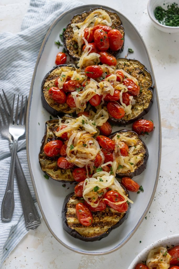 baked eggplant steaks on an oval plate with tomatoes and onions