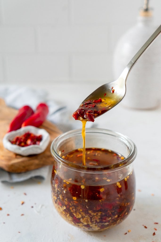 a spoon with chili garlic sauce over a glass jar